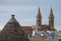 Conical roof of trulli house in Alberobello, Puglia, Italy, with the spires of Alberobello Cathedral in the background. Royalty Free Stock Photo