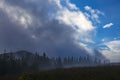 Coniferous forest in the mountains in the fog and the blue sky breaking through the clouds Royalty Free Stock Photo