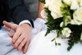 Connected hands of happy newlyweds without ring with bridal bouquet