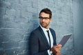 Connectivity unlocks doors. a handsome young businessman using his tablet while standing against a grey facebrick wall.