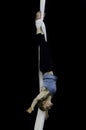 A female acrobat suspends herself upside down by wrapping aerial silks around her ankles