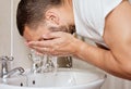 Consistent skincare will leave you glowing. a young man washing his face in his bathroom sink.