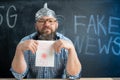 Conspiracy and a man sits at the blackboard and holds a sign 5g in his hands. Chalk board in the background with place