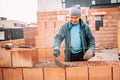 Construction bricklayer worker building house walls with bricks, mortar and rubber hammer