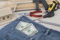 Construction and business concept. Different working tools, dollars in the pocket of jeans on wooden background.