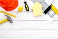 Construction concept. Helmet, tools on work desk, house cutout on white wooden background top-down frame copy space Royalty Free Stock Photo