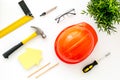 Construction concept. Helmet, tools on work desk, house cutout on white wooden background top-down pattern