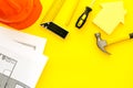 Construction concept. Helmet, tools on work desk, house cutout on yellow background top-down frame copy space