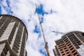 A construction crane on the background of the construction of two houses or skyscrapers and blue sky with clouds Royalty Free Stock Photo