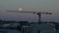 Construction crane in Reykjavik with full moon laying on it at sunset in Iceland
