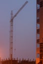 Construction crane on the site, unfinished house, fog covers the upper floors, evening twilight