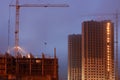 Construction crane on the site, unfinished multi-storey houses, fog covers the upper floors, evening twilight