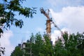 A construction crane works against a background of blue sky and green trees. The construction of a high-rise building with an Royalty Free Stock Photo