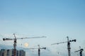 Construction cranes on the background of a clear sky and a large moon.