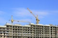 Construction cranes and a house frame on a blue sky. Royalty Free Stock Photo