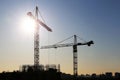 Silhouettes of construction cranes on unfinished residential building against the sky and shining sun