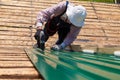 Construction elderly worker install new roof, Roofing tools, Electric drill used on new roofs with Metal Sheet. Self-made house by Royalty Free Stock Photo