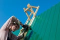Construction elderly worker install new roof, Roofing tools, Electric drill used on new roofs with Metal Sheet. Self-made house by Royalty Free Stock Photo
