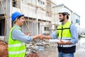 Construction engineer and architect with blueprint shaking hands while standing on construction site. Home building concept Royalty Free Stock Photo