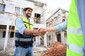 Construction engineer and architect with blueprint shaking hands while standing on construction site. Home building concept Royalty Free Stock Photo