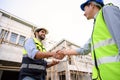 Construction engineer and architect with blueprint shaking hands while standing on construction site. Home building concept Royalty Free Stock Photo