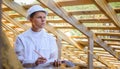 Construction engineer or architect with blueprints on building site of wood frame house. Portrait of a man in a white helmet with Royalty Free Stock Photo