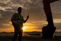 Construction engineer holding radio communications with backhoe in construction site by the sea at sunset. Royalty Free Stock Photo