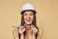 Construction girl in a white hard hat and protective construction mask holding a caliper. makes the measurement of the smile