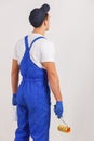 A construction guy in a uniform, looks at the wall, holding a building roller and a can of paint.