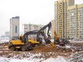 Construction of high-rise buildings in winter. The work of excavators. Land works. Digging pits. Concrete building frames