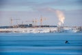 Construction of houses on a frosty sunny day. Cranes and frames of houses on the banks of the river covered with ice and snow. Royalty Free Stock Photo