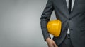 Construction industry business - businessman holding yellow hard hat underarm on gray background