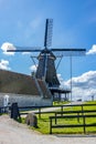 Construction next to a windmill located on a small hill with green grass and a path between fences