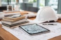 Construction Planner's Desk with Drafts, Tablet, Helmet, and Engineering Books Royalty Free Stock Photo