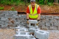 In construction plase, a worker lifts concrete blocks and positions them on retaining walls.