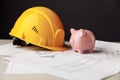 Construction safety helmet and piggy bank with blueprint Royalty Free Stock Photo