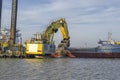 The construction of the seaport. A large floating excavator loads the barge with soil