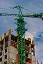 Construction site of apartment building with Crane of green color and copy-space on cloudy sky