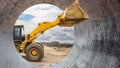 A construction site is bustling with activity as a large yellow excavator operates, viewed through a circular pipe. Loader, Royalty Free Stock Photo