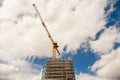 Construction site in a city with tall crane against blue cloudy sky. Frame of the building is in scaffolding without safety net. Royalty Free Stock Photo