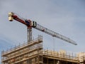 Construction site in a city with tall crane against blue cloudy sky. Frame of the building is in scaffolding without safety net. Royalty Free Stock Photo