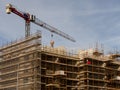 Construction site in a city with tall crane against blue cloudy sky. Frame of the building is in scaffolding without safety net. Royalty Free Stock Photo