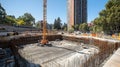 construction site with deep excavation pit and crane surrounded by urban buildings and green trees on a clear sunny day Royalty Free Stock Photo