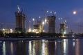 Construction site with cranes for high rise buildings at river. Night blue sky with half moon. City life style Royalty Free Stock Photo