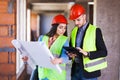 Construction site engineers with blueprints and tablet wearing hard hats Royalty Free Stock Photo