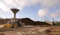 A construction site features a large, yellow tractor with a front loader on sandy terrain Royalty Free Stock Photo