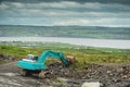Construction site in a field with blue color excavator working. Dark dramatic sky, West of Ireland