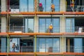 Construction site with a group of workers installing windows in a new building. They are using cranes and lifts to reach