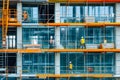 Construction site with a group of workers installing windows in a new building. They are using cranes and lifts to reach