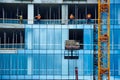 Construction site with a group of workers installing windows in a new building. They are using cranes and lifts to reach